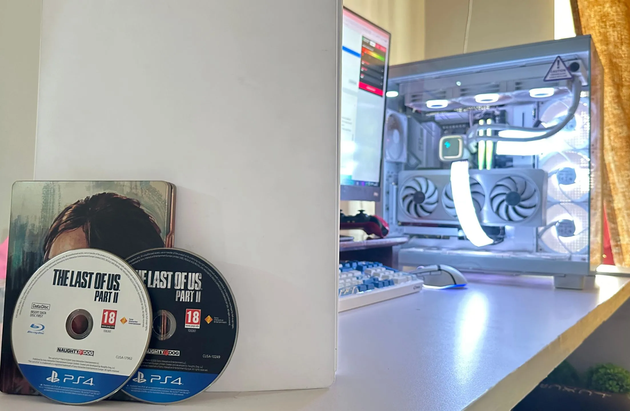 Hai đĩa game The Last of Us Part II phiên bản PS4 cùng với máy tính và PS5, minh họa dung lượng game lớn và sự bất tiện của đĩa vật lý.