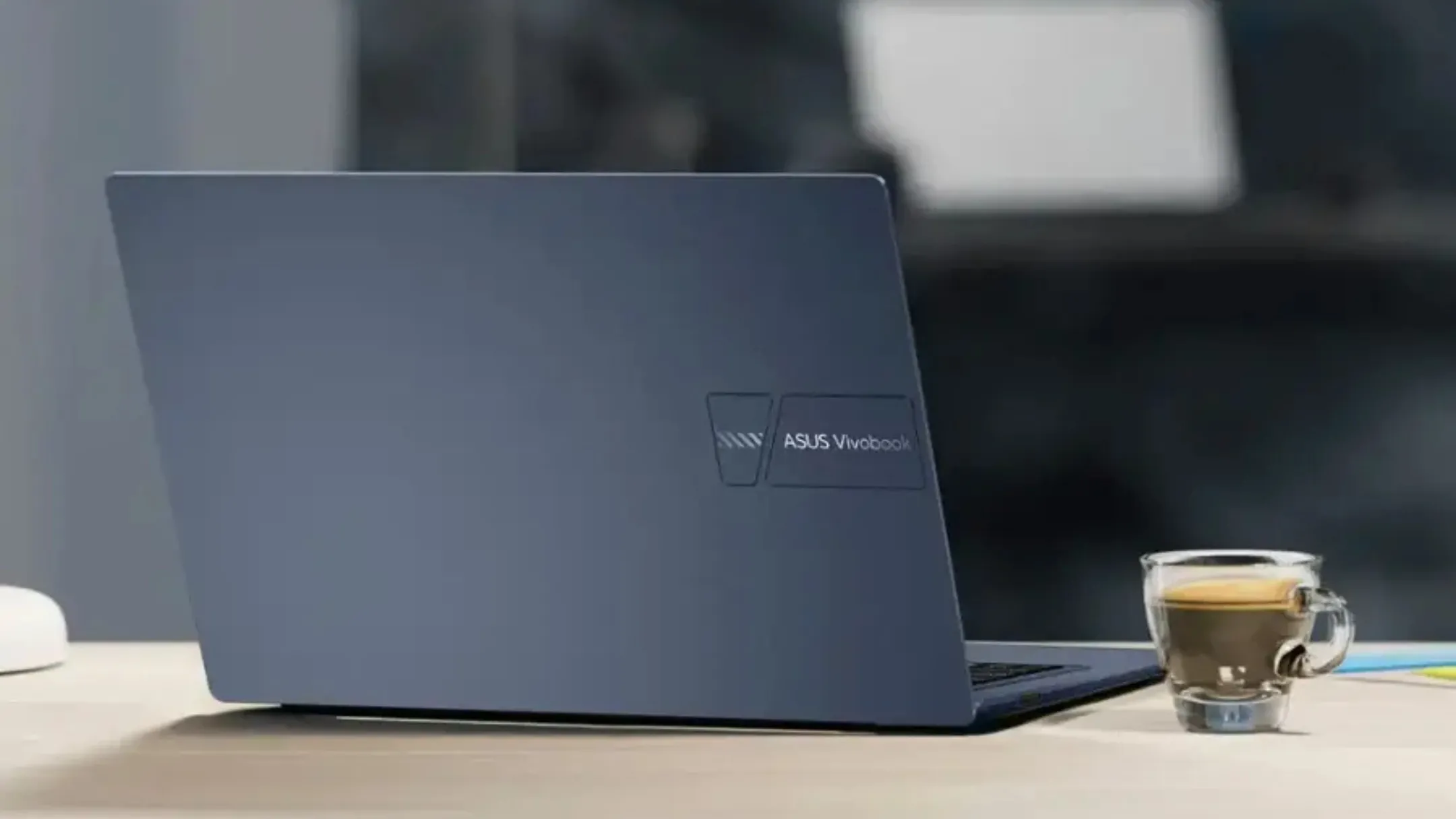 Laptop Asus Vivobook 14 trên bàn làm việc cạnh ly cà phê, thể hiện khả năng làm việc di động.