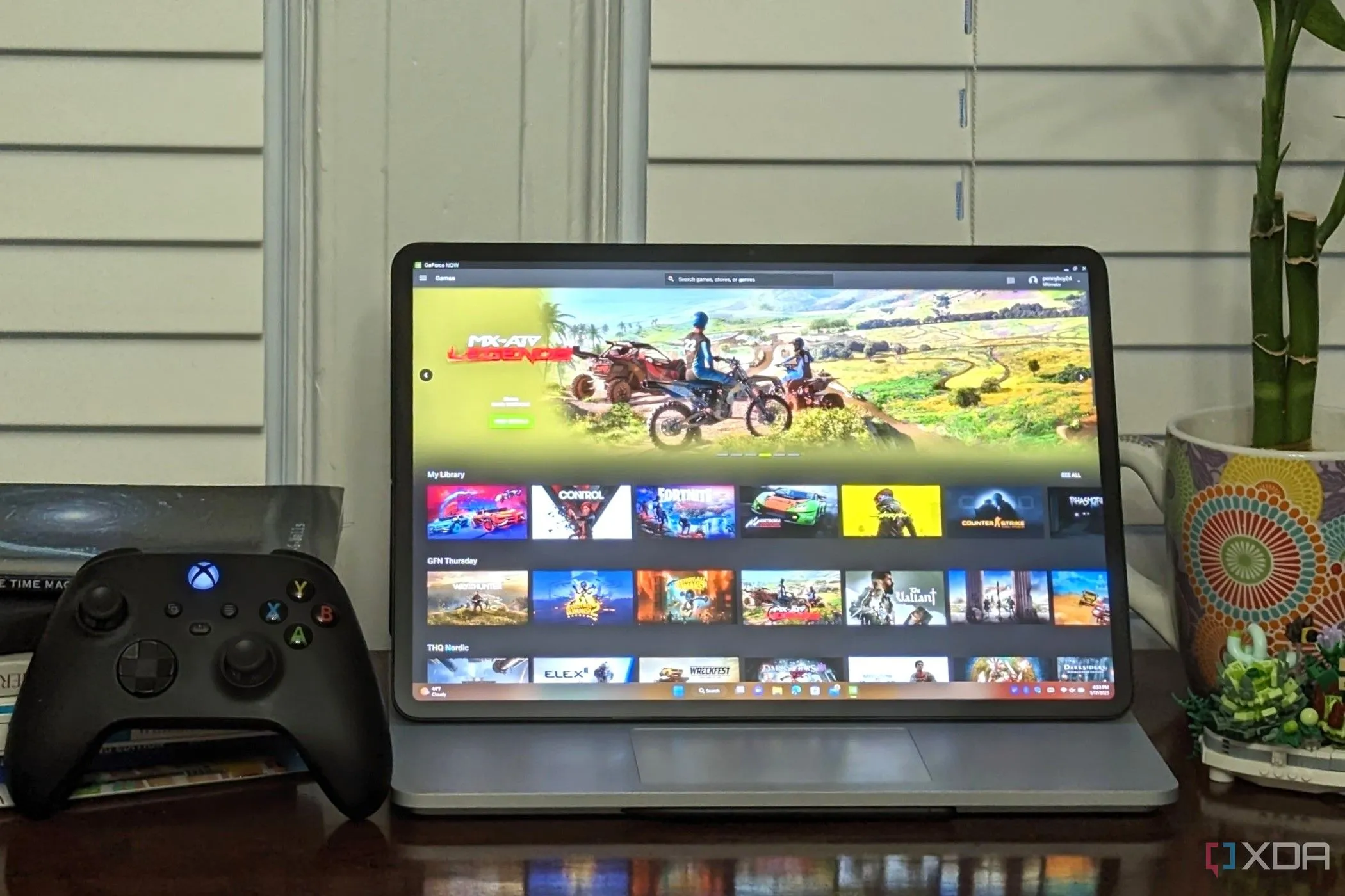 Laptop đang chạy dịch vụ Nvidia GeForce Now Ultimate, cạnh đó là bộ điều khiển Xbox