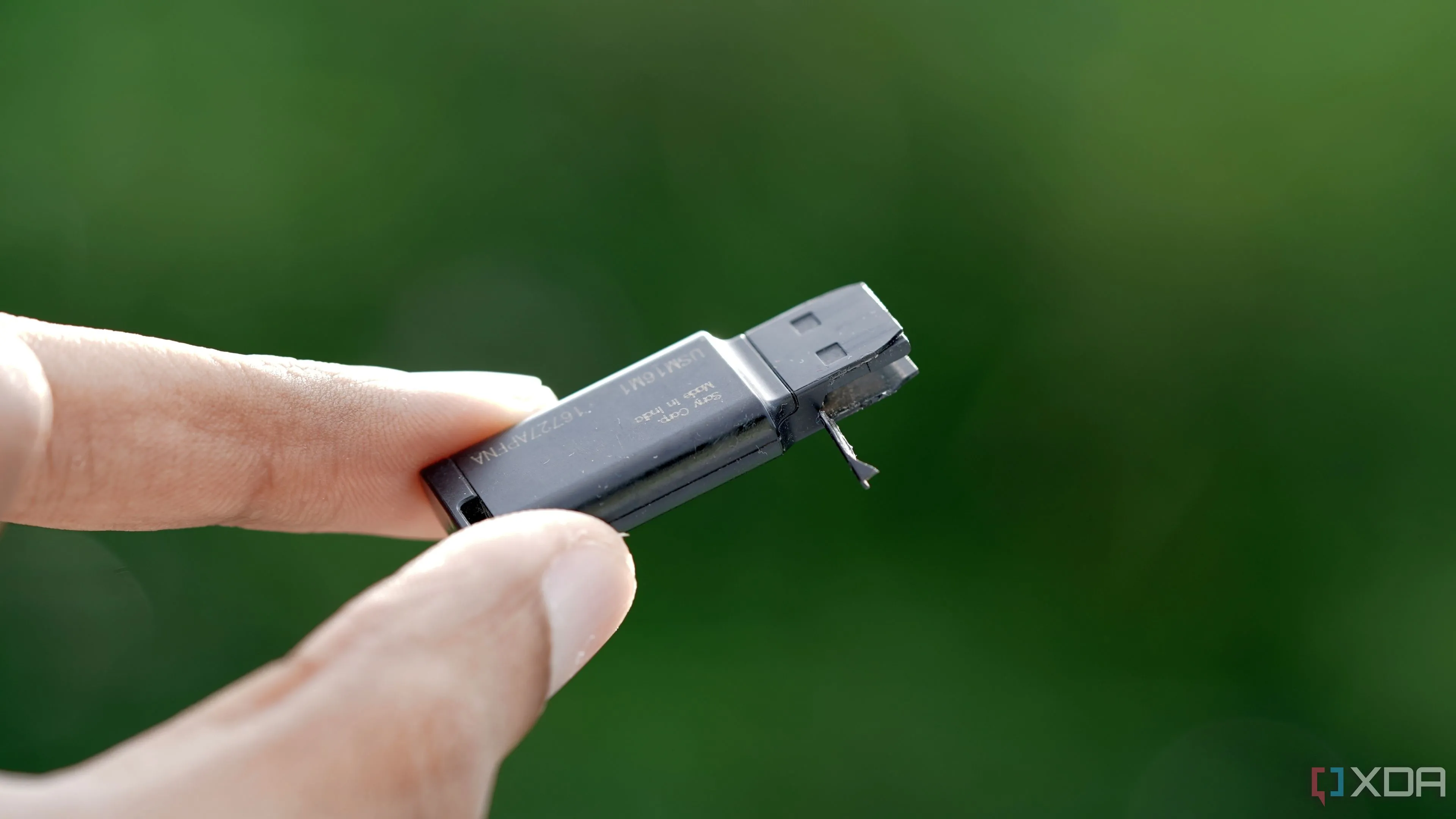 Một chiếc USB flash drive Sony 16GB màu đen đã bị hỏng, đặt trên nền xanh lá cây tươi tốt
