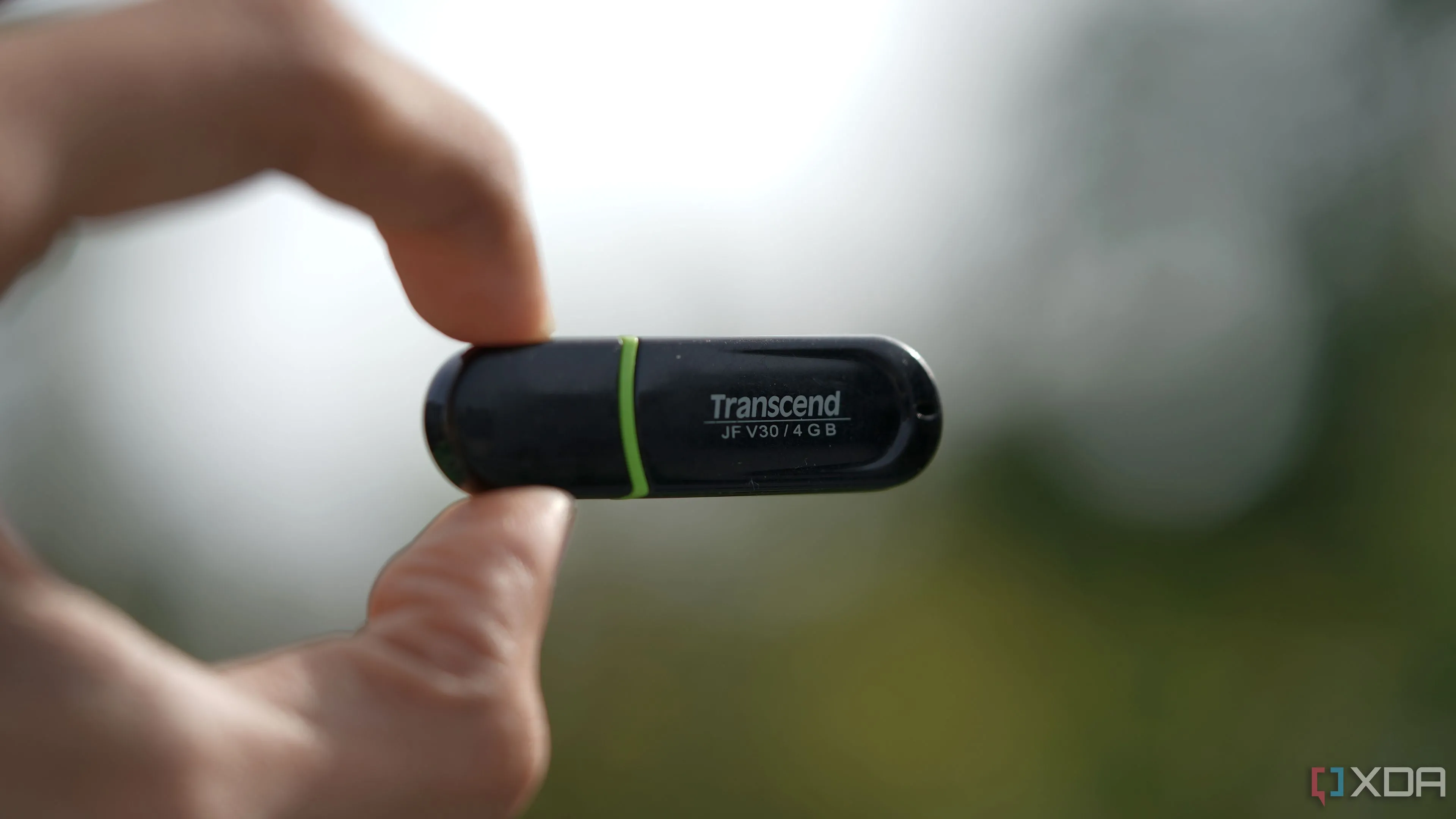 Một chiếc USB Transcend 4GB được giữ bằng hai ngón tay trên nền mờ