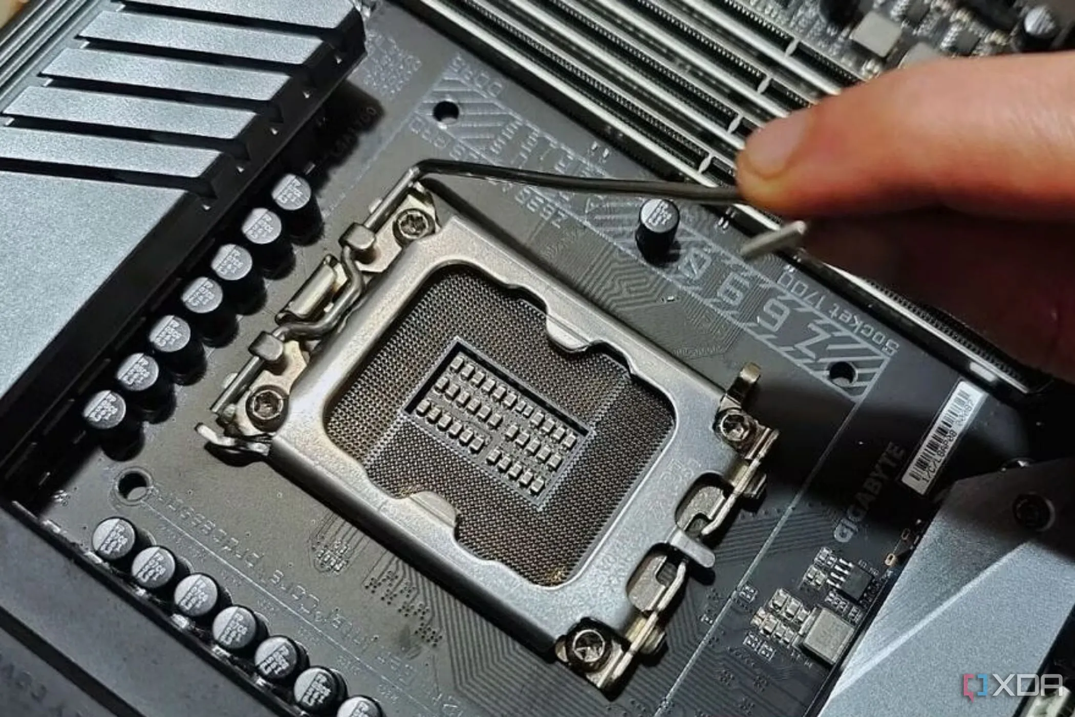 Người dùng đang cầm cần gạt kim loại gần socket CPU trên bo mạch chủ, thể hiện thao tác liên quan đến socket.