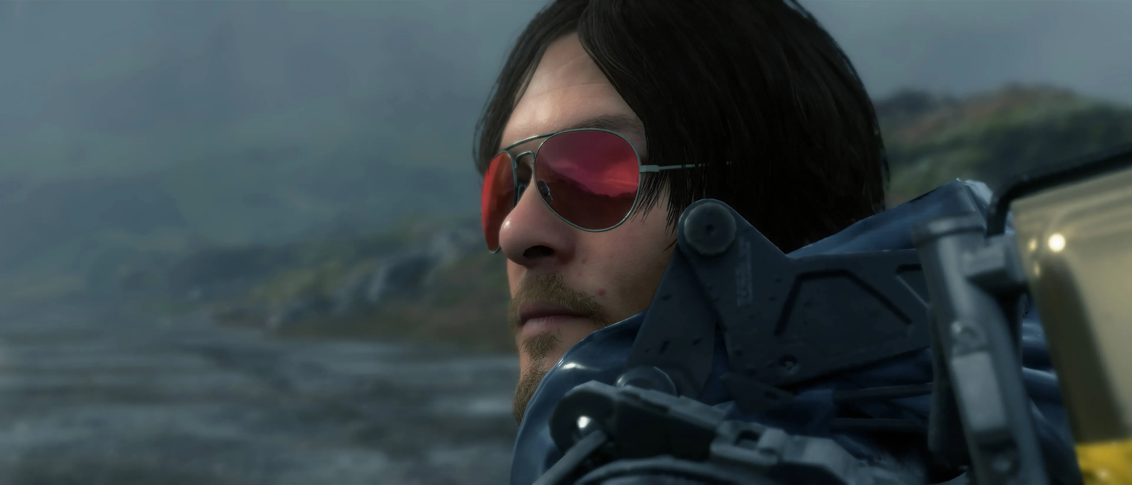 Sam Porter Bridges đeo kính râm trong game Death Stranding, thể hiện phong cách của người giao hàng qua vùng đất hoang tàn.